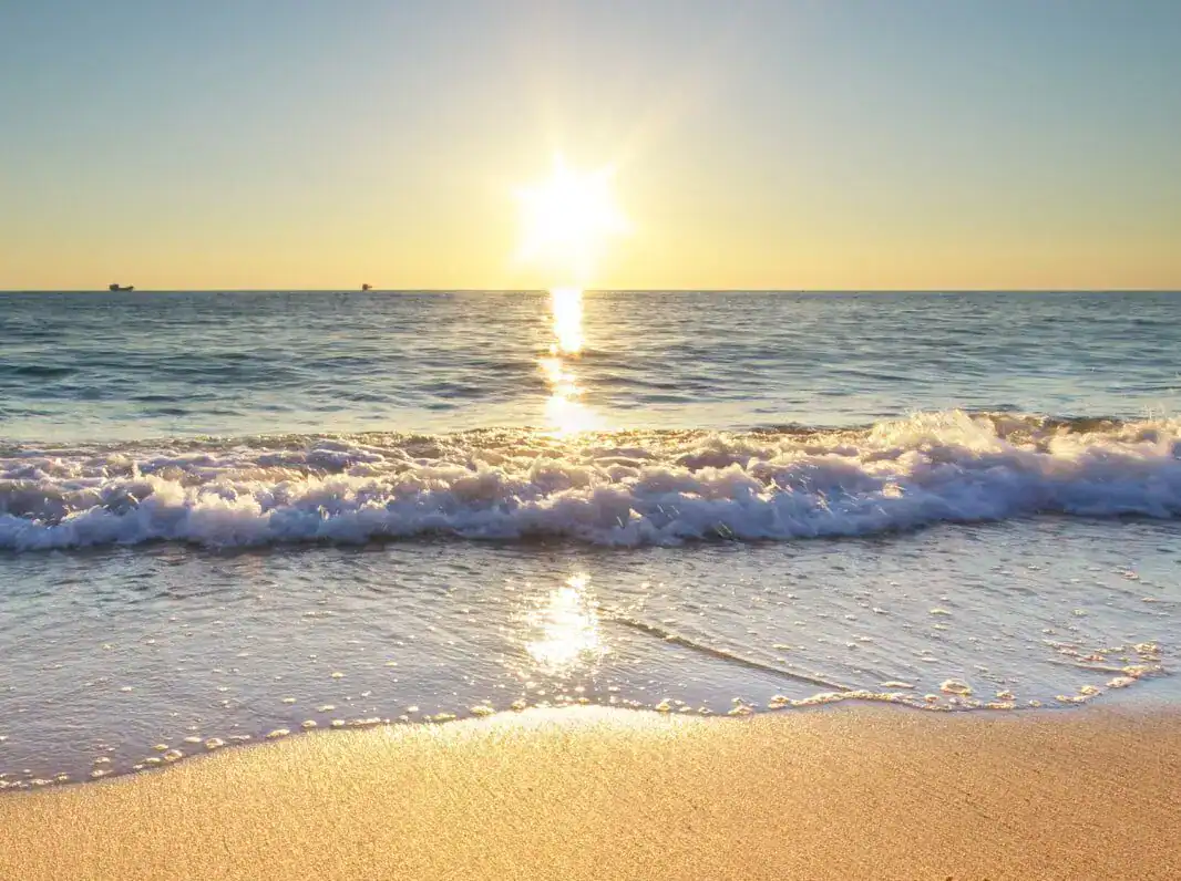 Sunrise over the ocean with gentle waves washing onto a sandy beach.