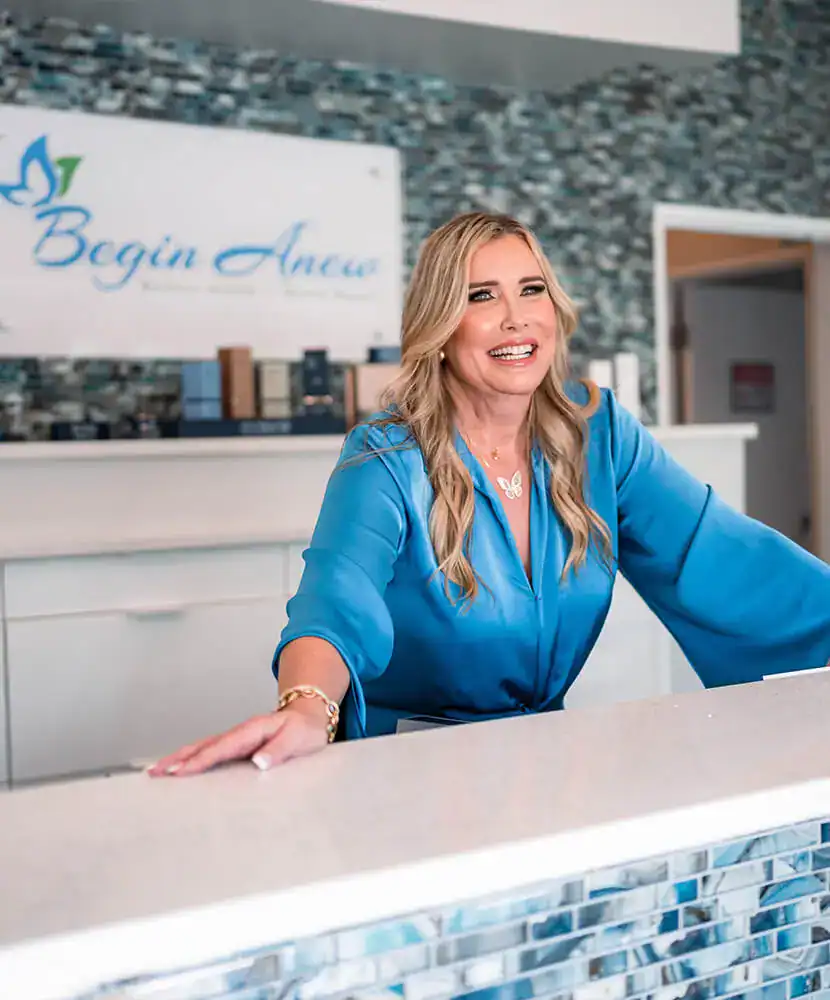 Friendly medical spa professional welcoming clients at the reception desk of Begin Anew.