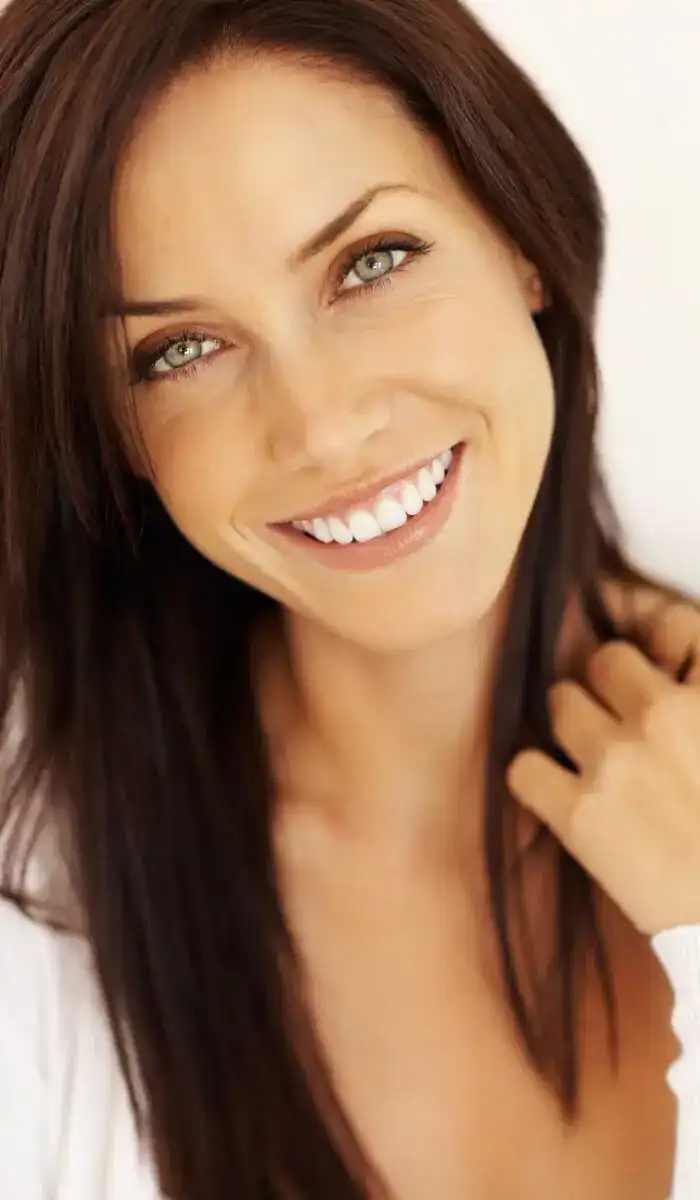 Smiling woman with clear, radiant skin and natural makeup in soft lighting.