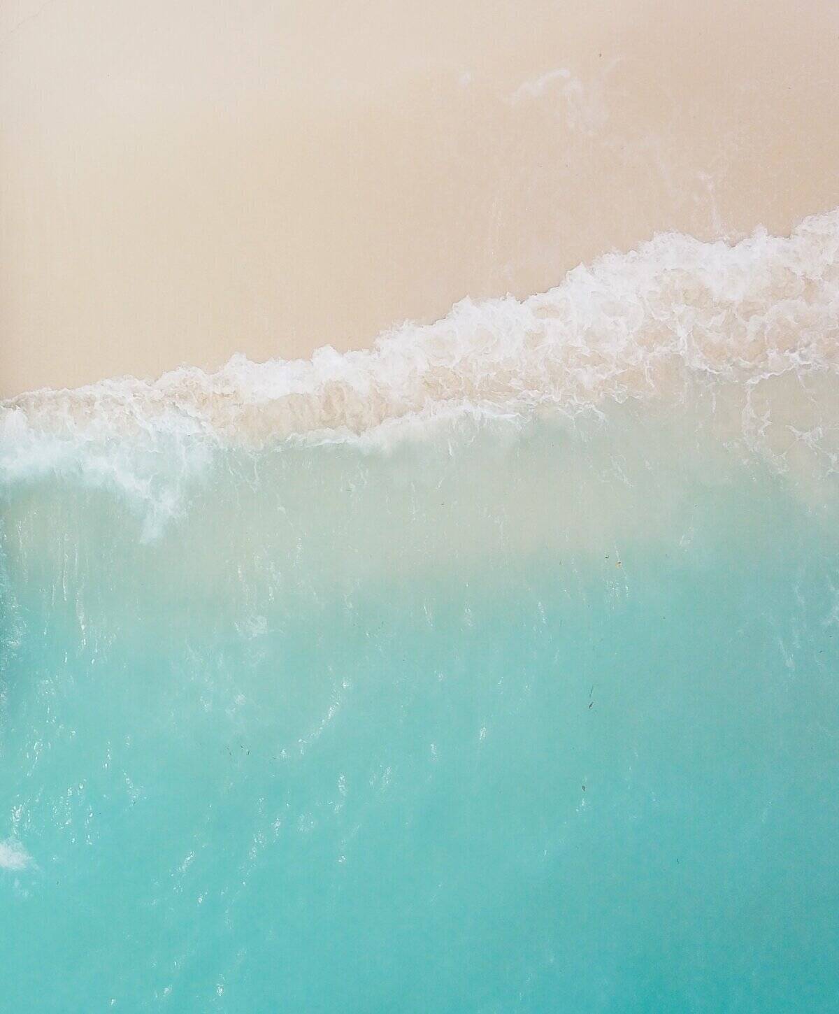 Aerial view of turquoise ocean waves meeting sandy beach