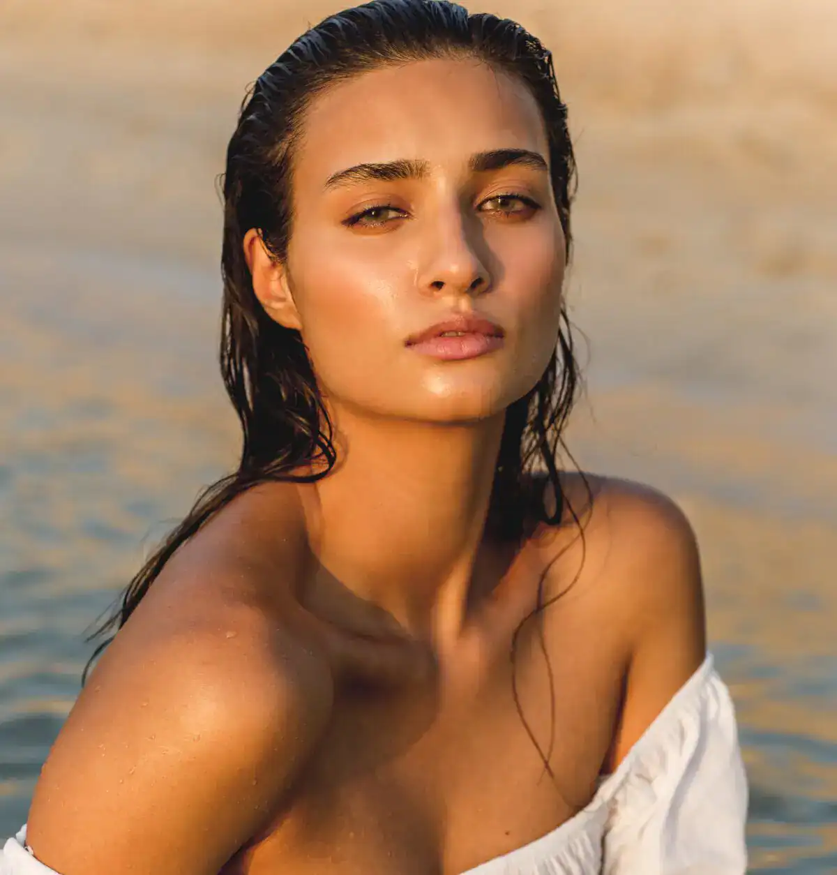 Close-up portrait of a woman with wet hair wearing a white off-the-shoulder top outdoors.