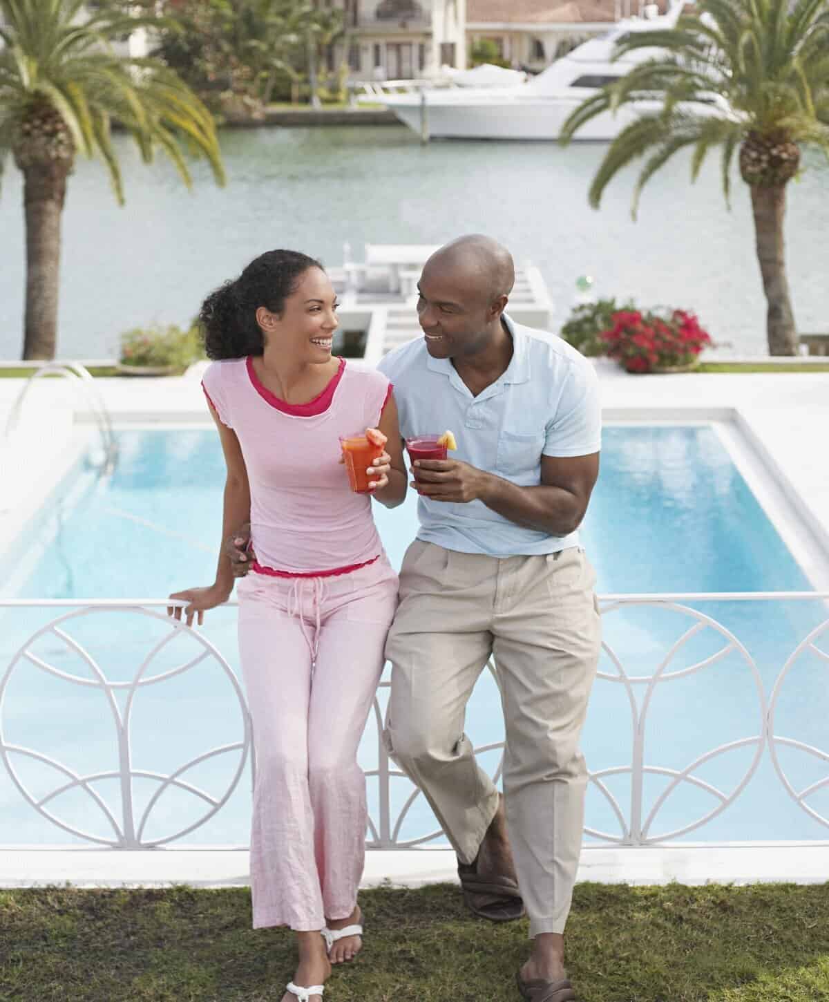 Smiling couple holding drinks beside a pool at a luxury home