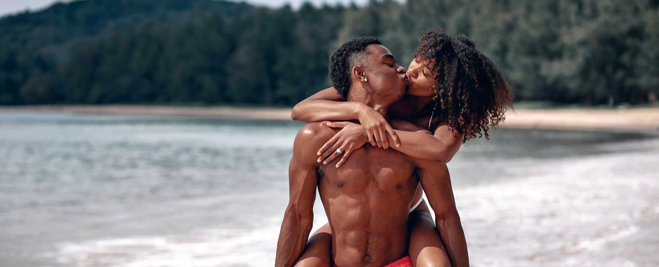 Couple embracing and kissing at the beach with ocean and forest background