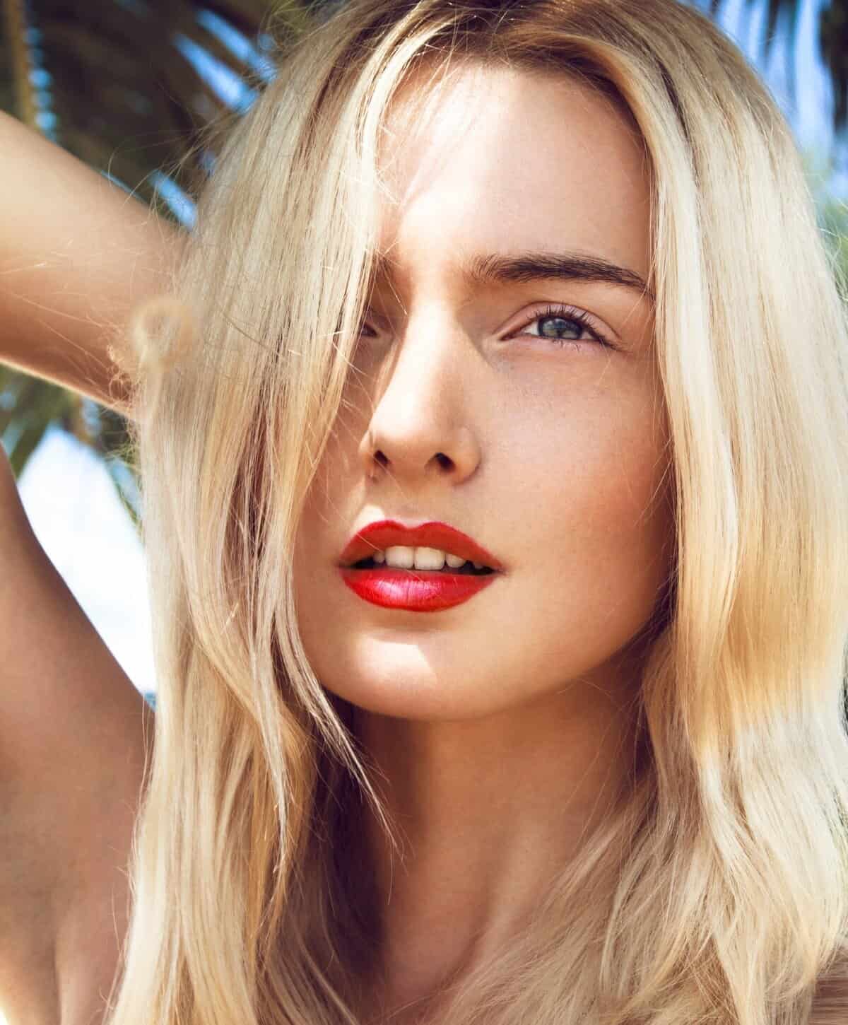 Close-up portrait of a blonde woman wearing red lipstick outdoors in natural light.