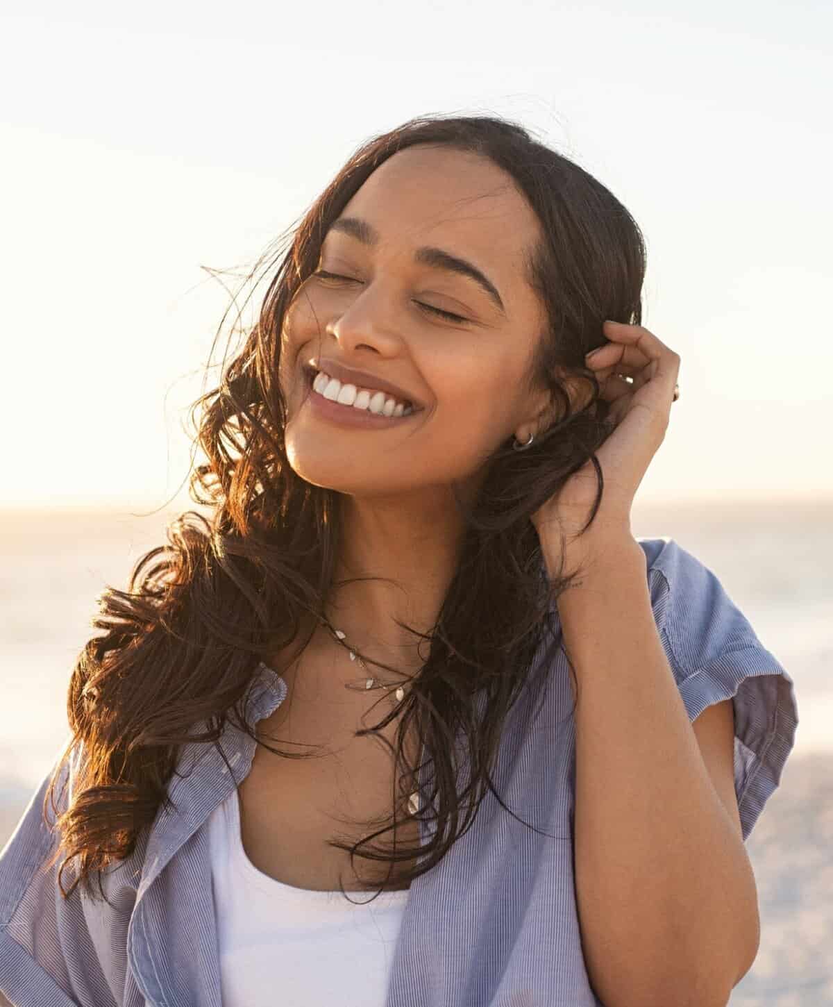 Close-up of a smiling woman with eyes closed enjoying natural sunlight.
