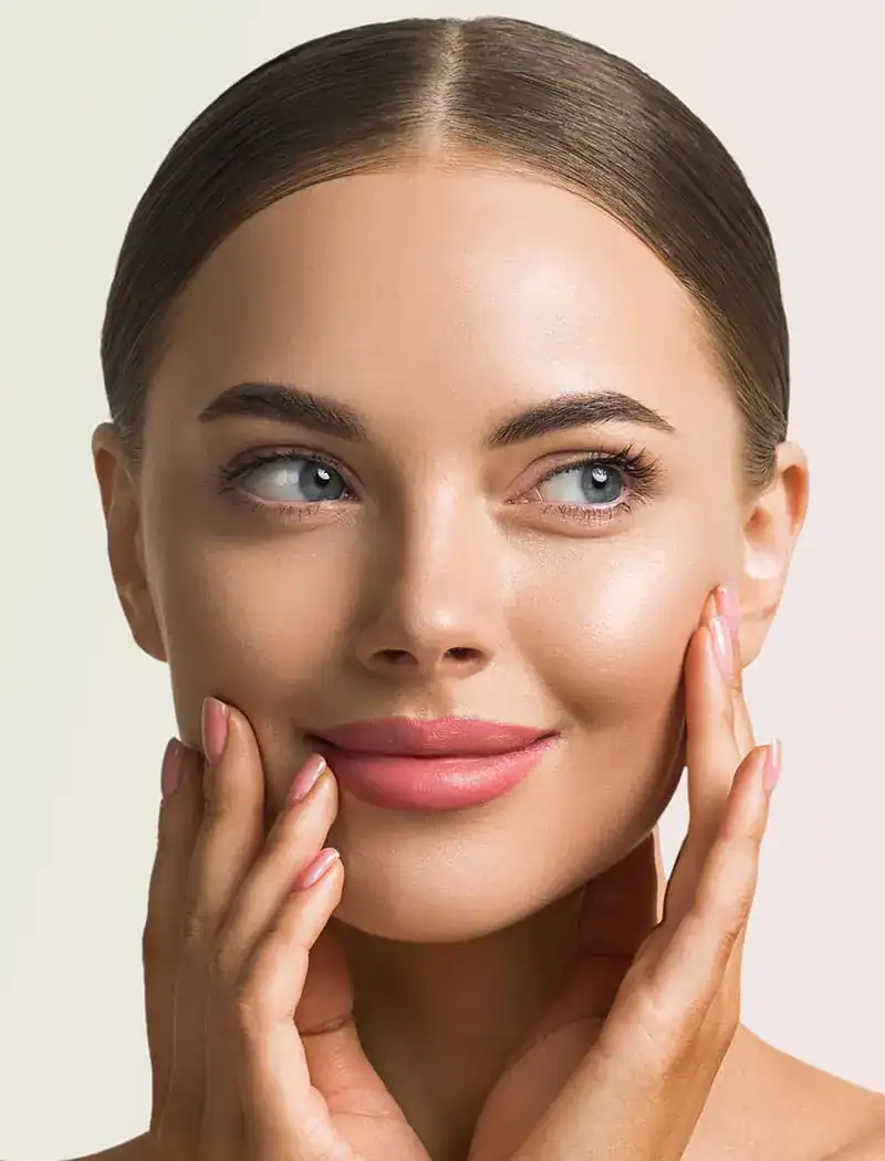 Close-up portrait of a woman with glowing, clear skin and pink lipstick touching her face to showcase professional skincare results.