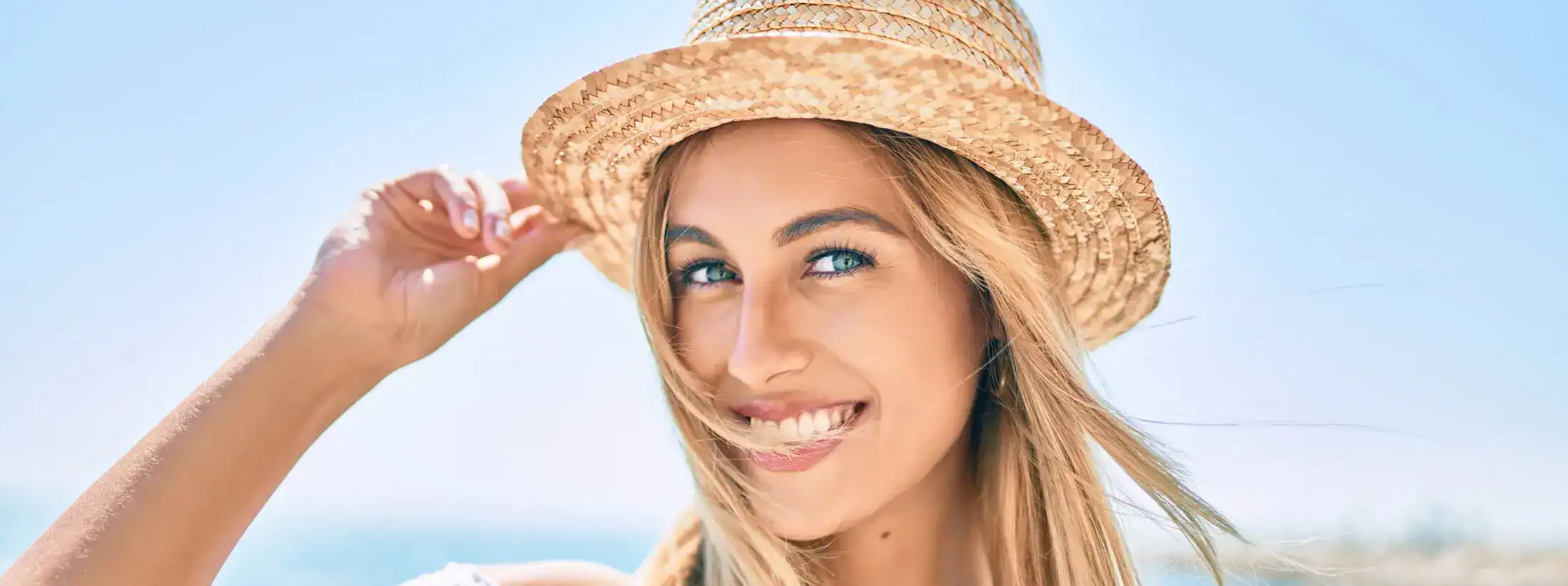 Smiling blonde woman wearing a straw sun hat on a bright sunny day at the beach.