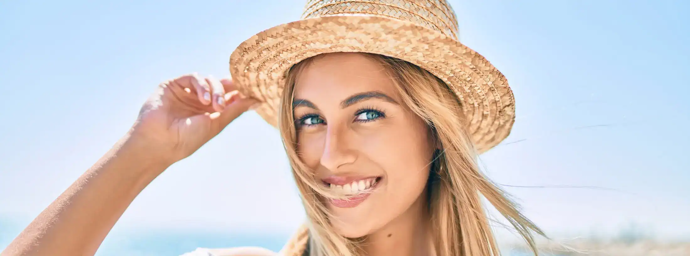 Smiling woman wearing a straw hat enjoying sunshine at the beach.