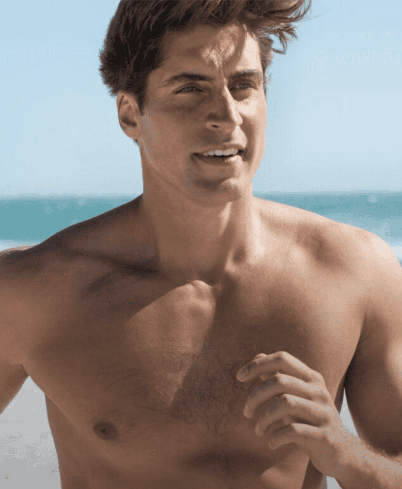 Fit man jogging along the beach with ocean waves in the background on a sunny day