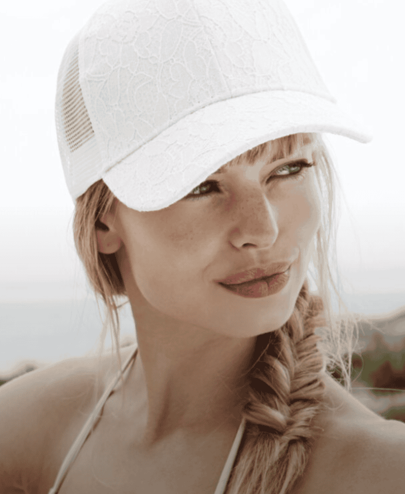 Woman with a blonde fishtail braid wearing a white lace baseball cap outdoors.