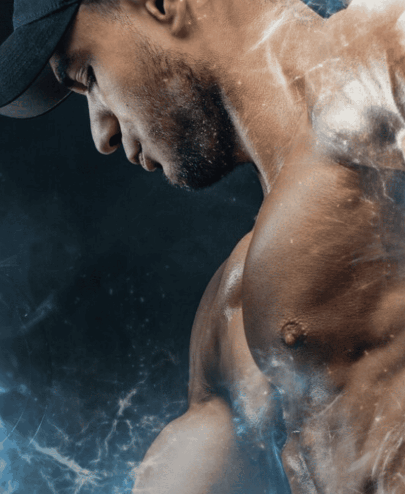 Muscular man in black cap posing in smoky gym lighting.
