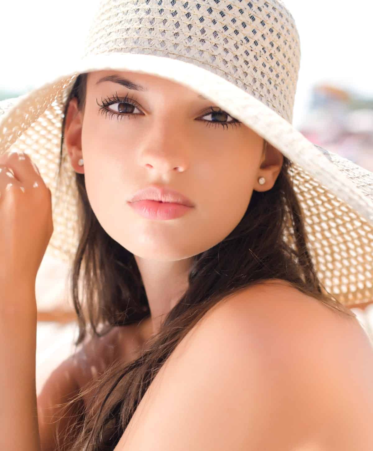 Young woman with smooth skin wearing a sun hat on a bright summer day.