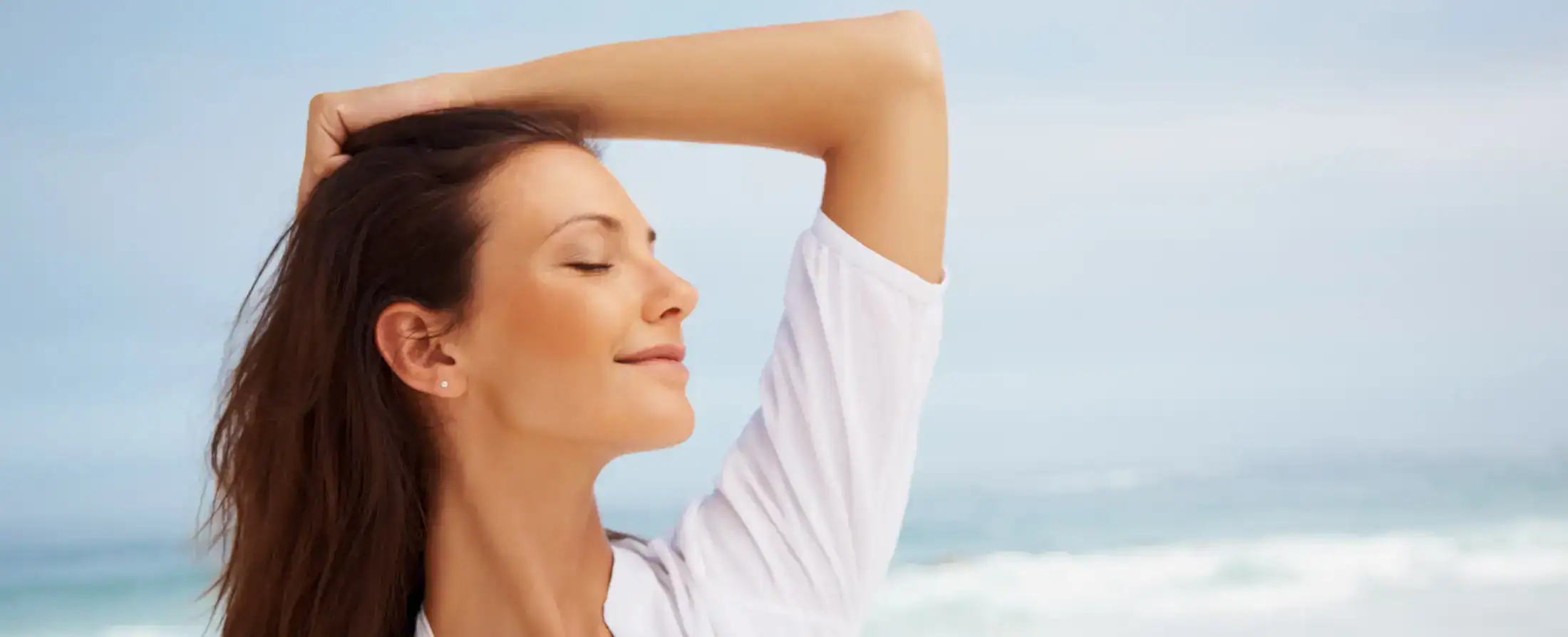 Woman with eyes closed enjoying the sun on a beach with a clear sky.
