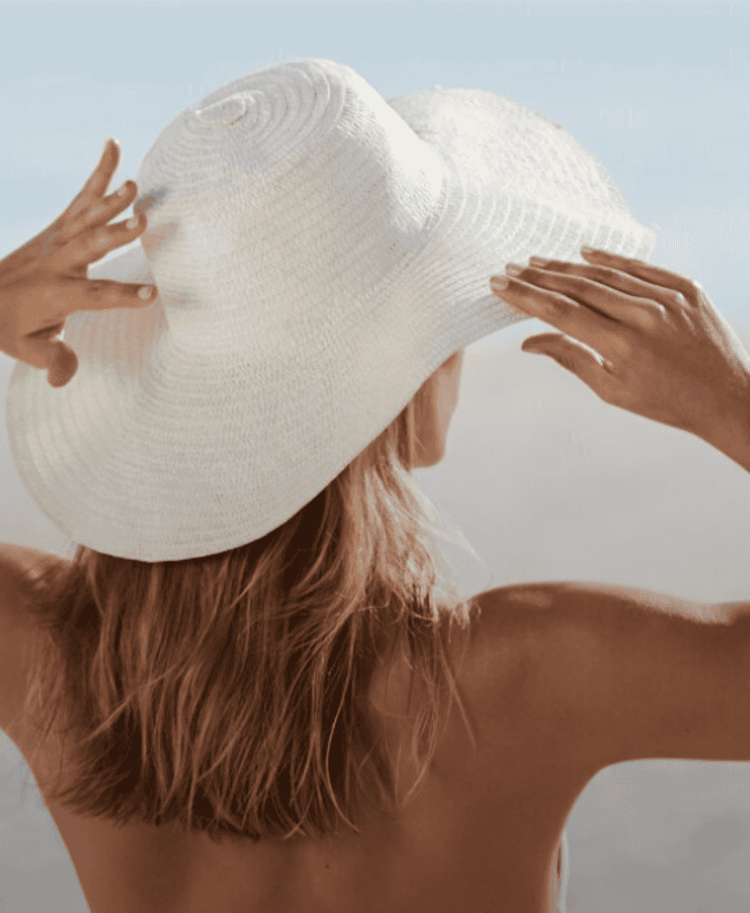 Woman adjusting a wide-brimmed white sun hat while standing outdoors in bright daylight