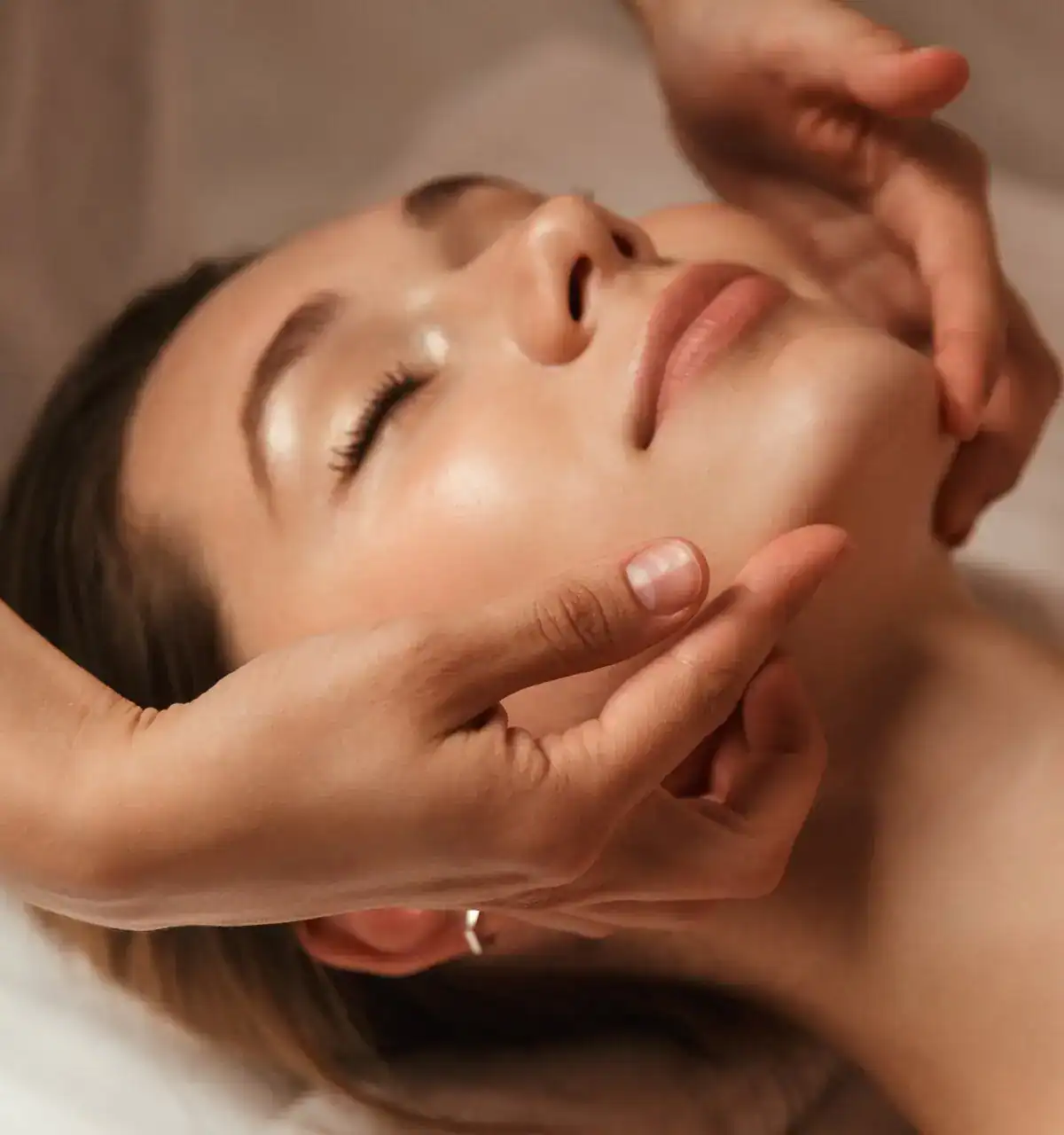 Woman receiving a professional face massage in a warm, soft-lit setting.