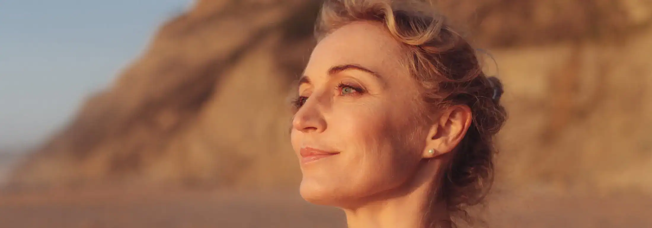 A close-up side profile of a woman with healthy, glowing skin looking toward the sunset, representing natural skincare and anti-aging results.