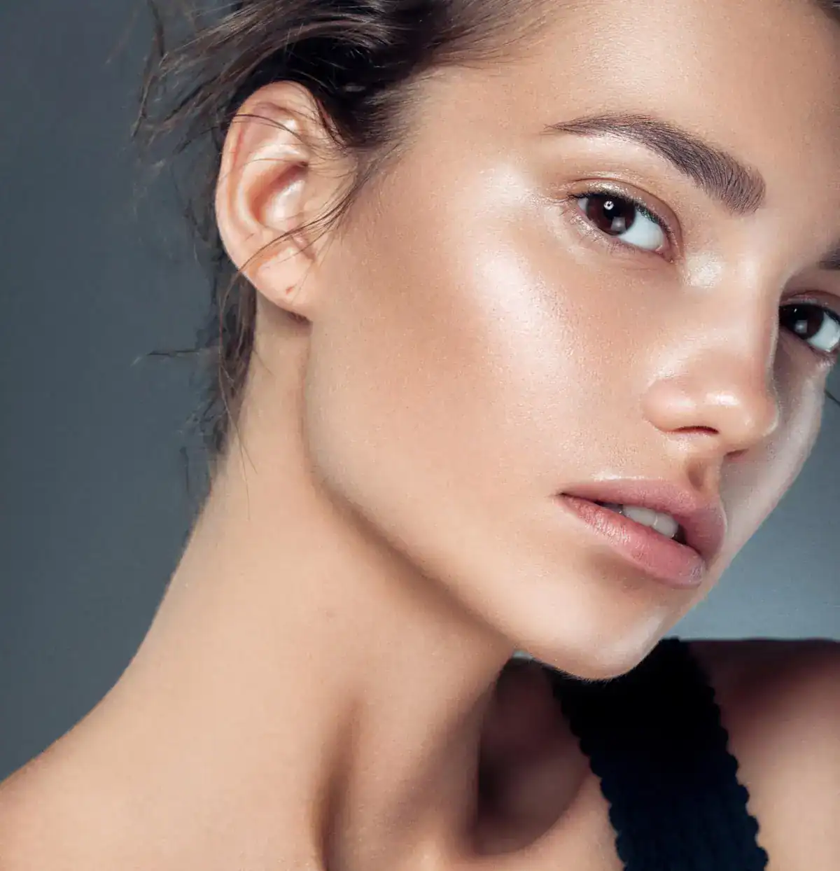 Close-up beauty portrait of a woman with radiant, dewy skin and natural makeup looking off-camera.
