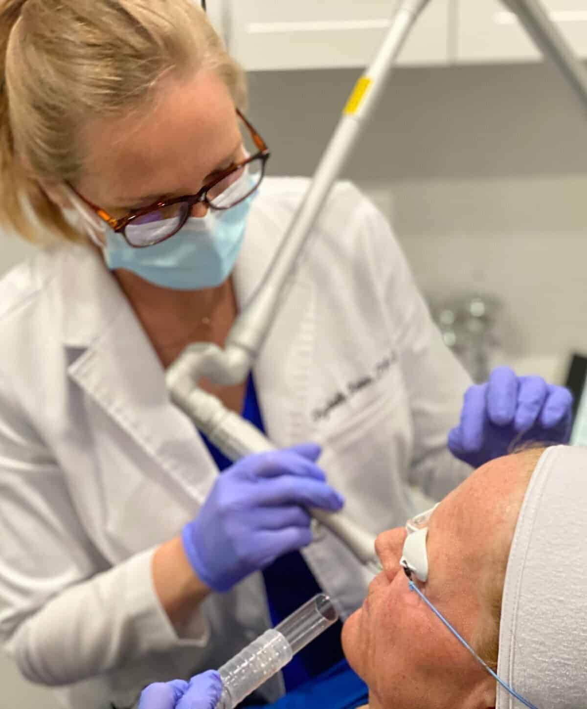 A medical professional performing a targeted laser skin treatment on a patient wearing protective eyewear in a clinical setting.