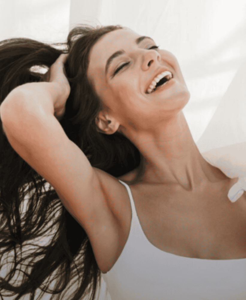 Happy young woman laughing with eyes closed and hair blowing in the wind against a white background.