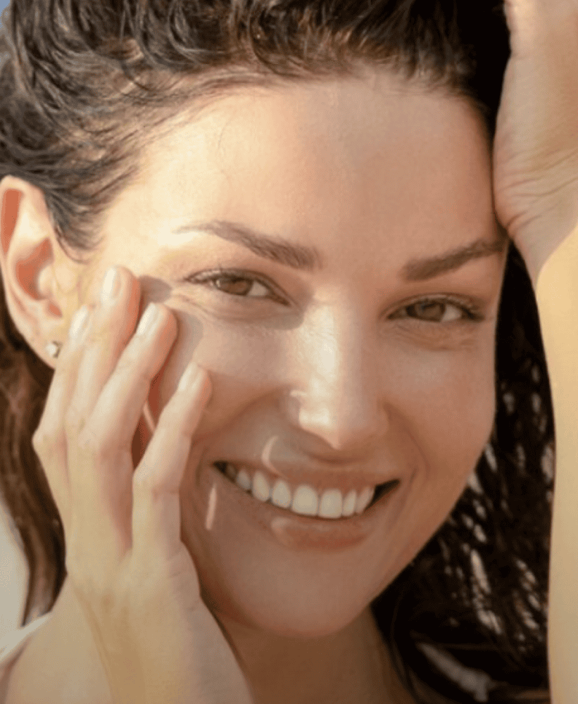 Smiling woman in natural sunlight with smooth, healthy-looking skin.