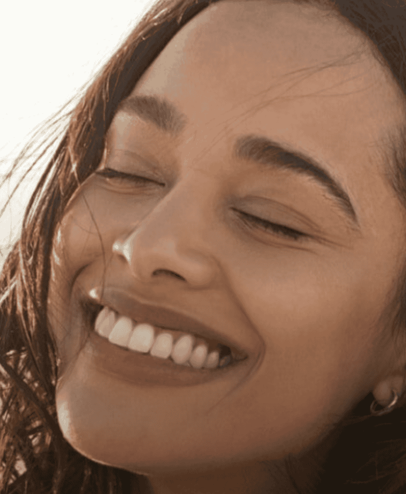 Close-up of a smiling woman with eyes closed enjoying natural sunlight.