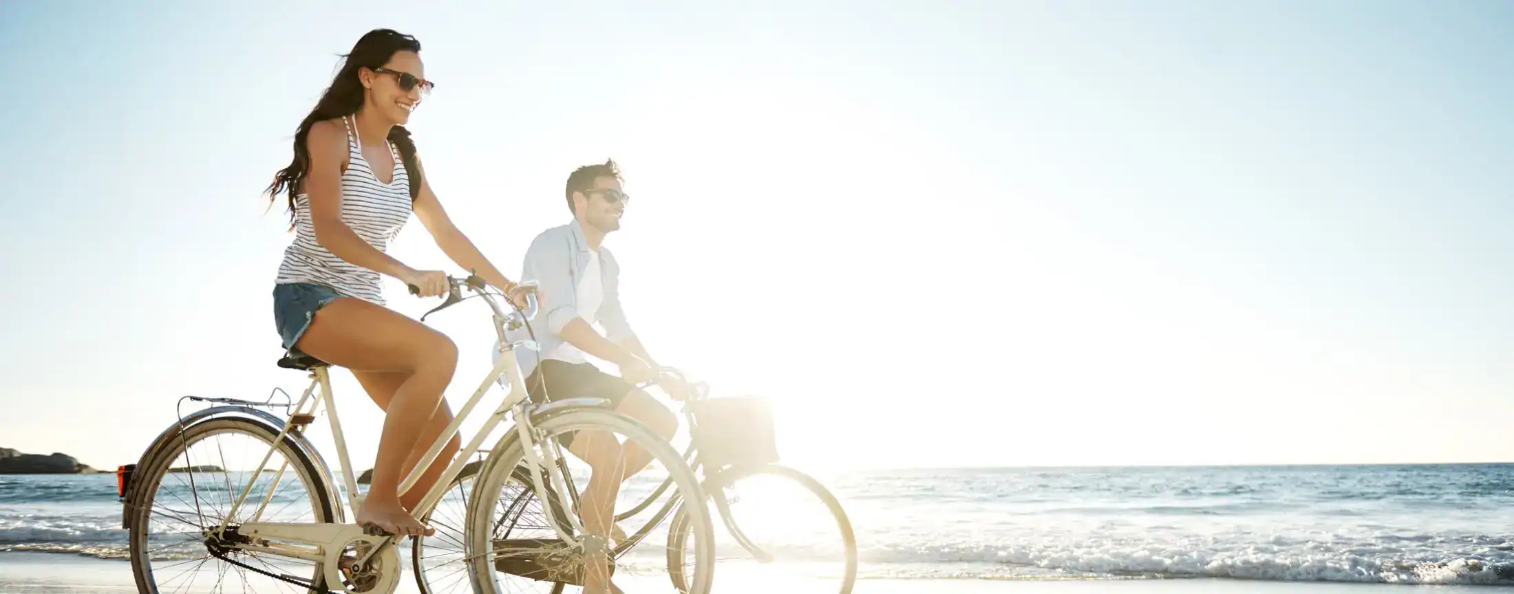 Happy young couple riding bicycles along a sunny beach shoreline.