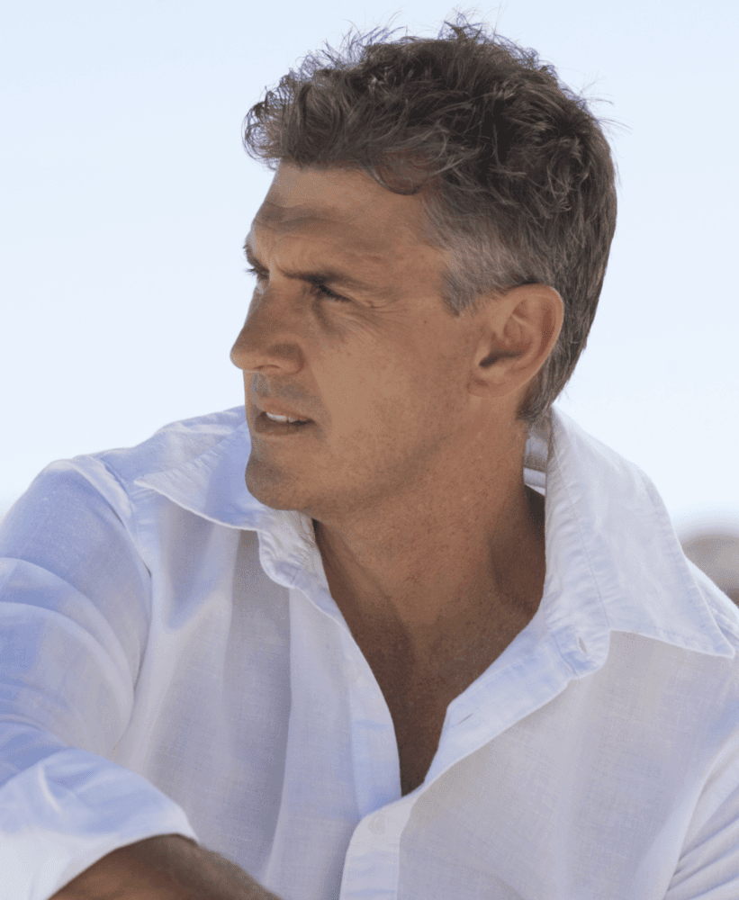 Man in a white shirt looking to the side outdoors in natural sunlight.