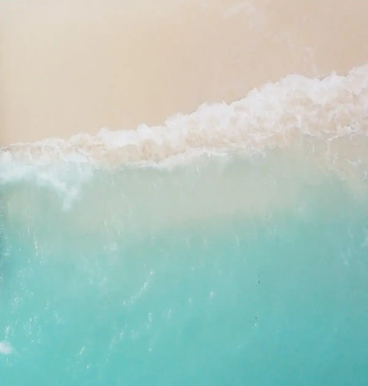 Aerial top-down view of turquoise ocean waves crashing onto a pristine white sand beach.