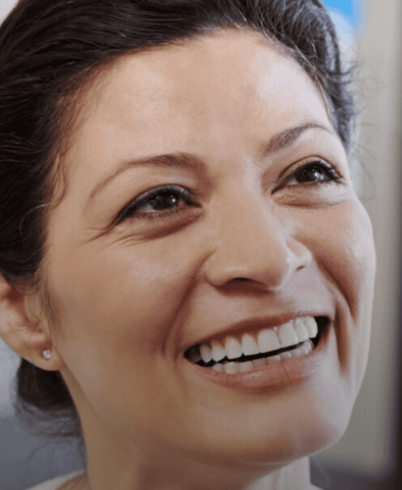 Close-up of a smiling woman with dark hair and white teeth looking upward.