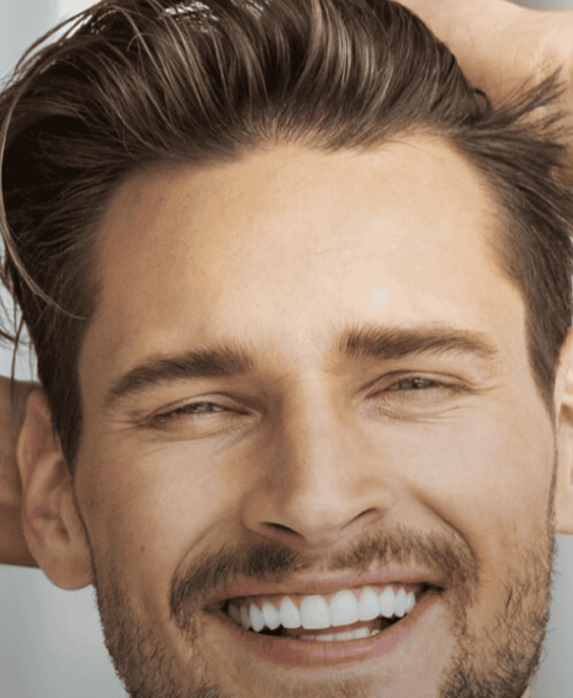 Close-up portrait of a smiling man with styled brown hair, groomed beard, and bright white teeth.
