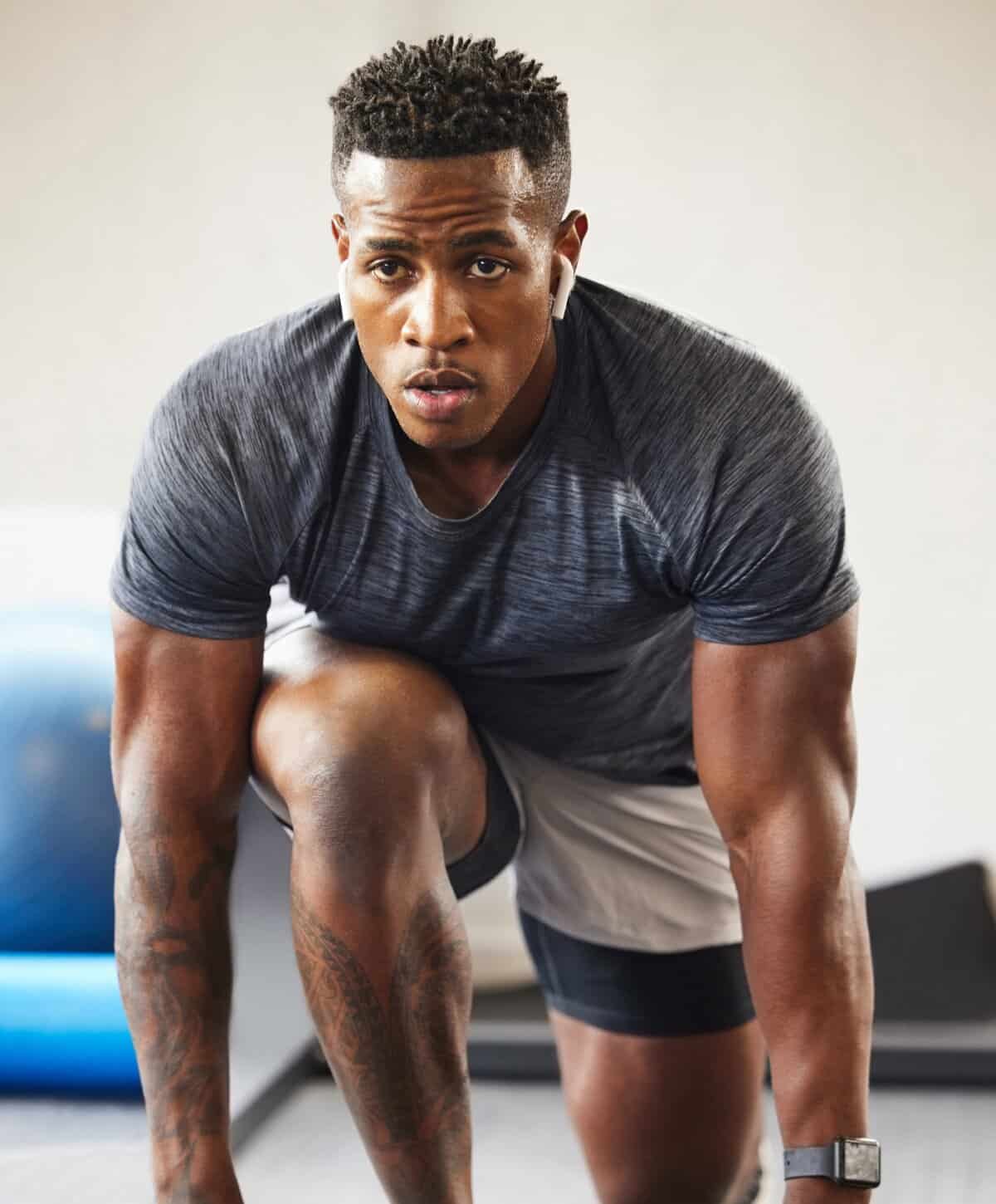 A muscular man in a gym wearing a grey workout shirt, focused and ready for a fitness training session.