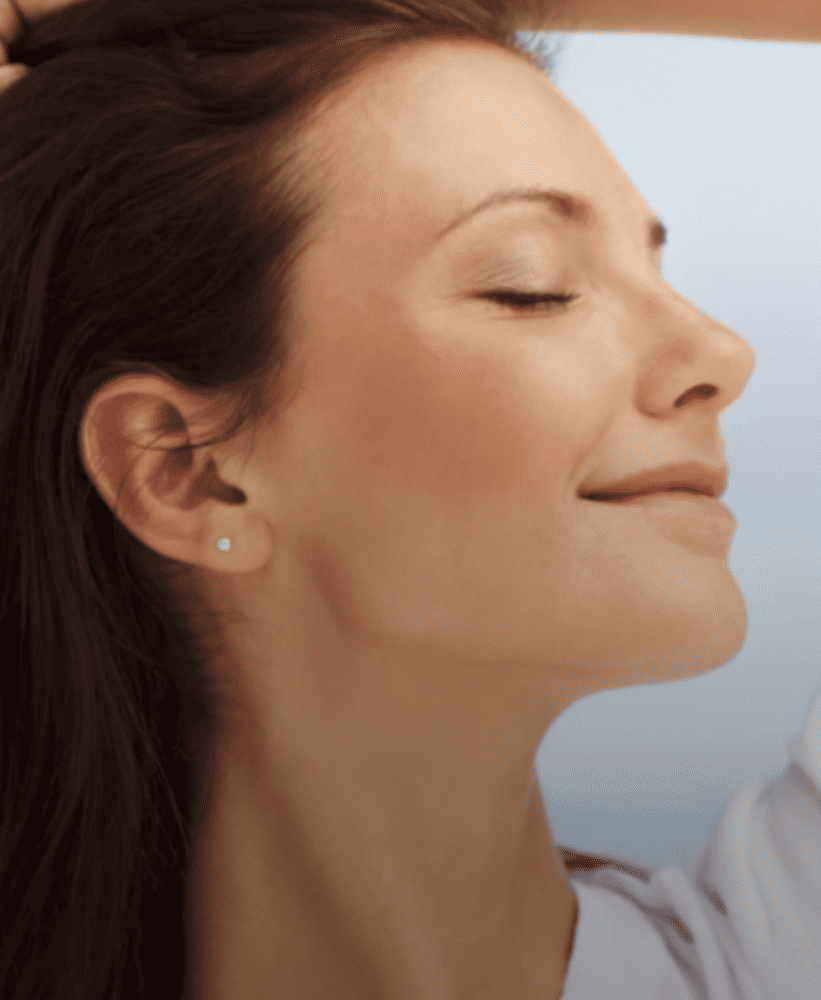 Profile of a smiling woman with dark hair and glowing skin against a light blue sky background.