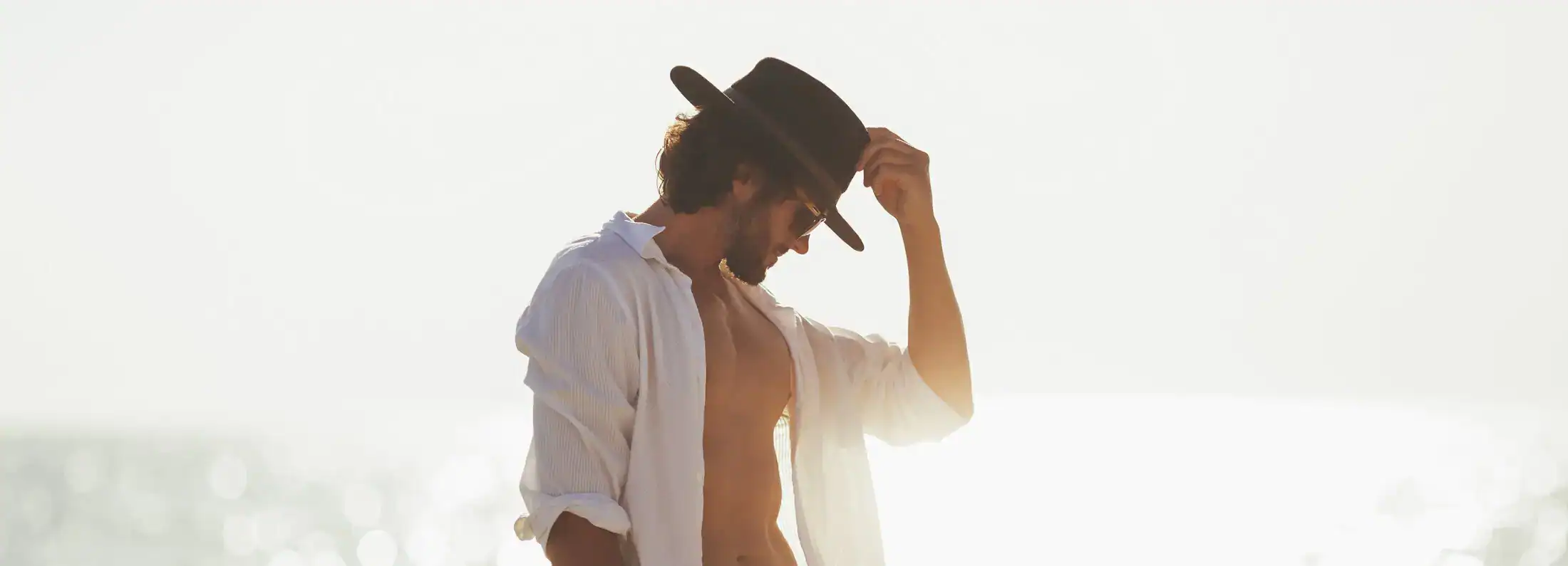 Man in white linen shirt and hat on beach representing male hormone health and vitality.