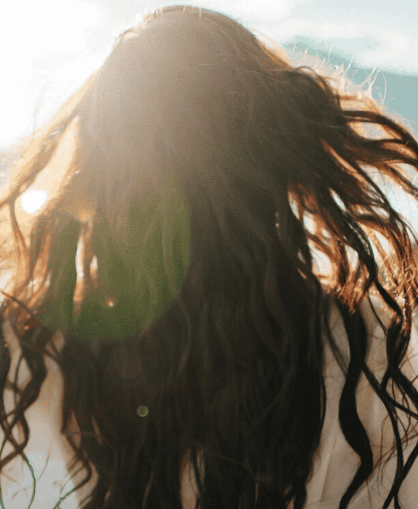 Woman with long flowing hair illuminated by sunlight, creating a soft natural glow outdoors