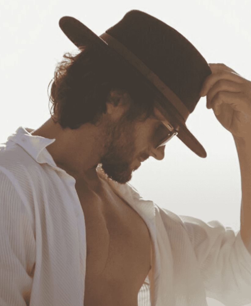 Stylish man wearing a hat and sunglasses enjoying a relaxed moment outdoors in warm sunlight