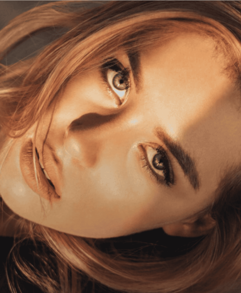 Close-up portrait of a woman's face with warm sunlight and detailed blue eyes.