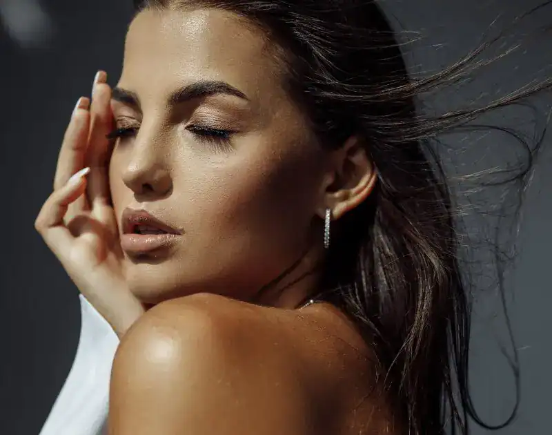 Brunette model with sun-kissed skin and neutral makeup posing with eyes closed.